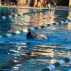 A swimmer with cerebral palsy, wearing a swim cap and goggles, takes a breath while racing down a lane in an outside pool.